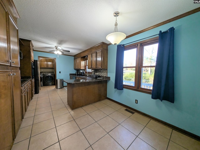 kitchen featuring pendant lighting, washer and clothes dryer, light tile patterned floors, tasteful backsplash, and kitchen peninsula