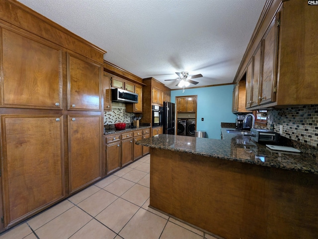 kitchen featuring black appliances, decorative backsplash, washing machine and dryer, dark stone countertops, and kitchen peninsula