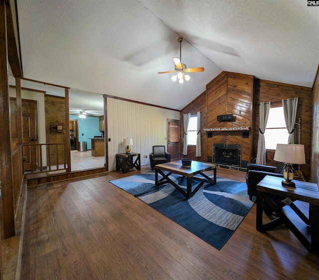 living room featuring ceiling fan, a large fireplace, wood-type flooring, lofted ceiling, and wooden walls