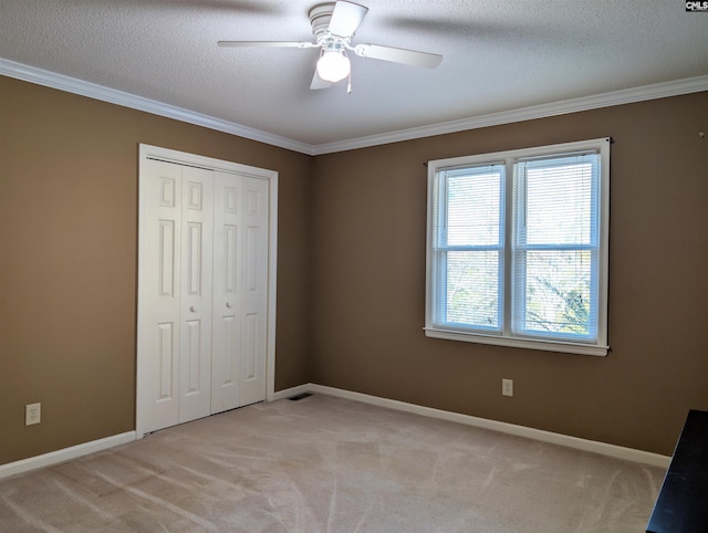 unfurnished bedroom with ceiling fan, ornamental molding, a textured ceiling, light colored carpet, and a closet