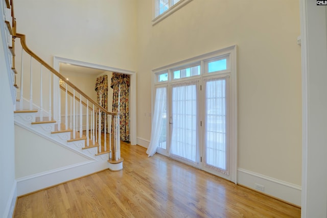 foyer featuring wood-type flooring, a towering ceiling, and french doors