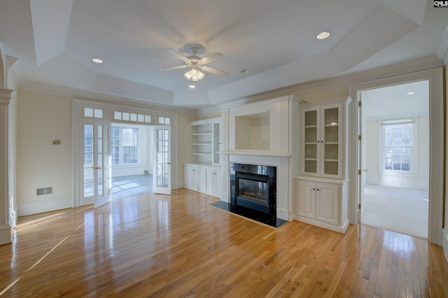 unfurnished living room with ceiling fan, light hardwood / wood-style floors, a premium fireplace, and a tray ceiling