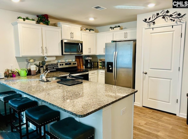 kitchen with white cabinets, light wood-type flooring, appliances with stainless steel finishes, kitchen peninsula, and a breakfast bar area