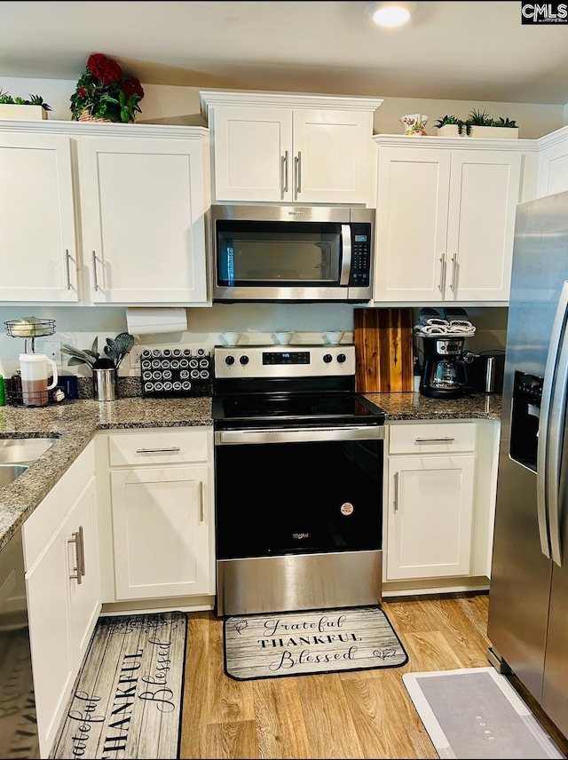 kitchen featuring stainless steel appliances, white cabinetry, dark stone countertops, and light hardwood / wood-style flooring