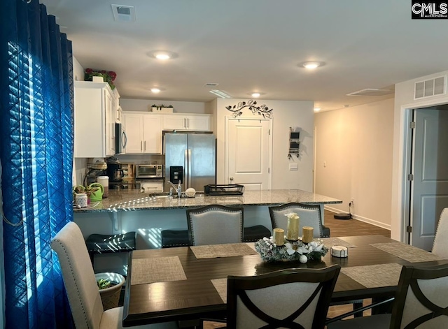 kitchen featuring light stone countertops, stainless steel appliances, a kitchen breakfast bar, backsplash, and white cabinets