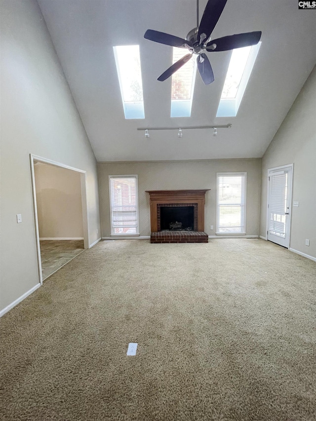 unfurnished living room featuring high vaulted ceiling, a skylight, ceiling fan, a fireplace, and carpet floors