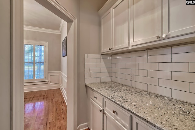 bar with backsplash, crown molding, light hardwood / wood-style flooring, light stone counters, and white cabinetry