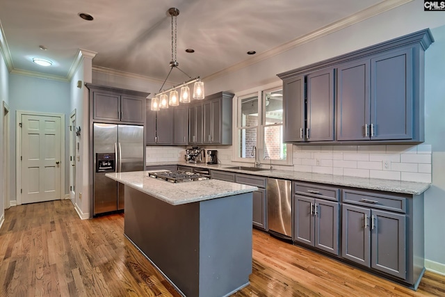 kitchen featuring sink, hanging light fixtures, stainless steel appliances, a kitchen island, and light wood-type flooring