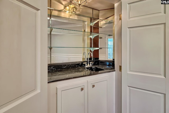 bar with white cabinets, crown molding, dark stone countertops, and sink