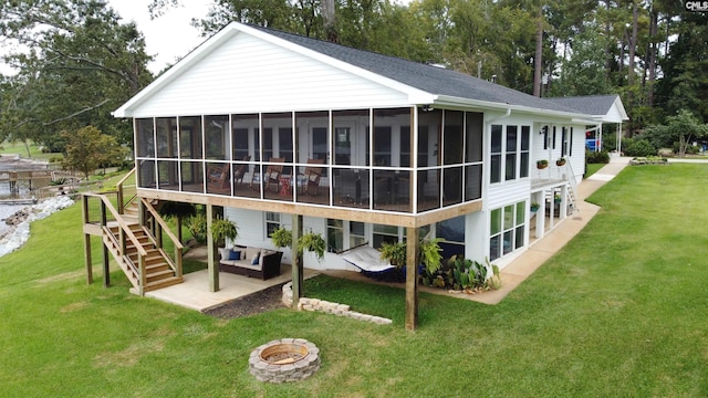 rear view of house with a sunroom, a yard, a patio, and an outdoor living space with a fire pit