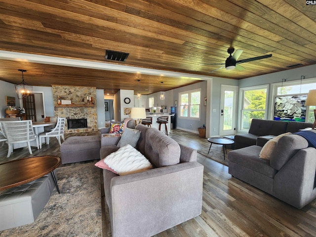 living room featuring ceiling fan with notable chandelier, a stone fireplace, dark hardwood / wood-style flooring, and wooden ceiling