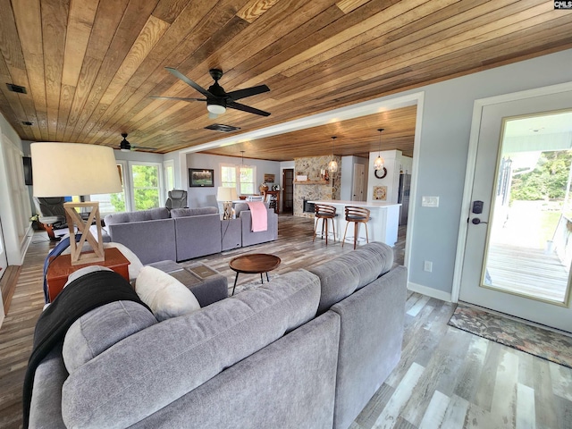 living room featuring hardwood / wood-style floors, ceiling fan with notable chandelier, a stone fireplace, and wooden ceiling