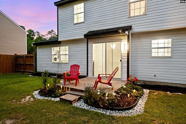 back house at dusk featuring a wooden deck and a yard