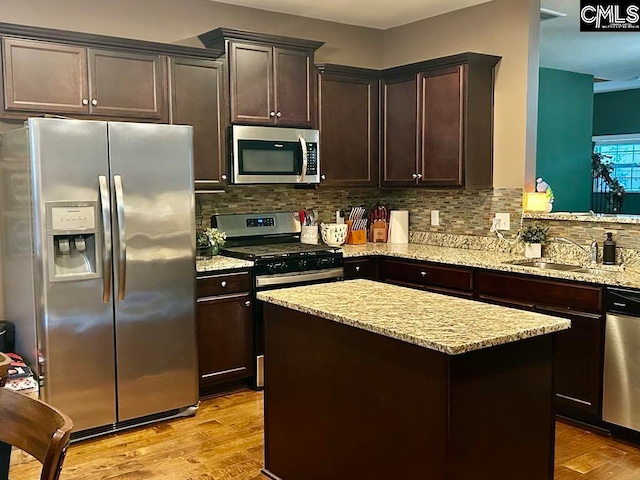 kitchen featuring a kitchen island, light stone countertops, tasteful backsplash, light hardwood / wood-style floors, and stainless steel appliances