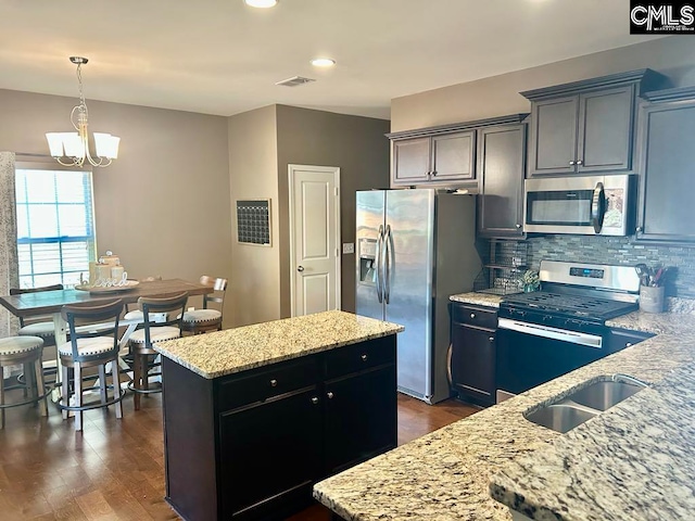 kitchen with a center island, stainless steel appliances, light stone counters, a chandelier, and decorative backsplash