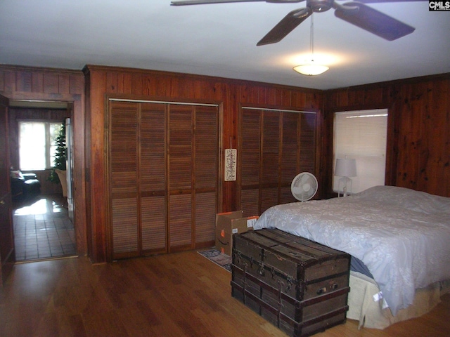 bedroom with wooden walls, dark hardwood / wood-style floors, ceiling fan, and multiple closets