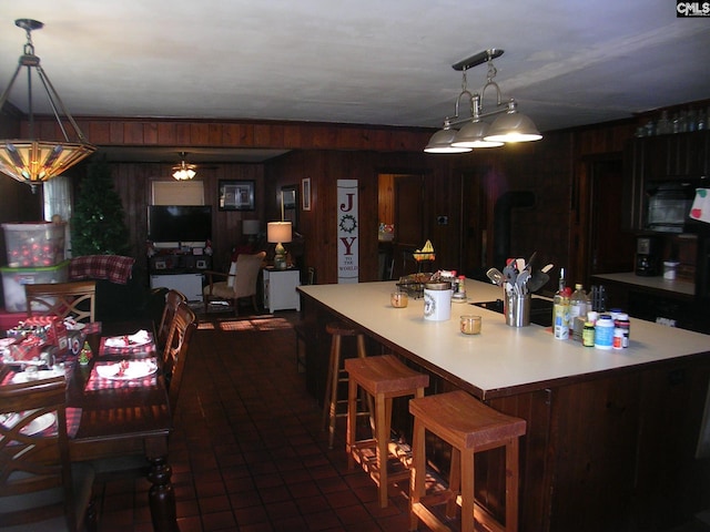 kitchen featuring dark tile patterned floors, pendant lighting, a center island, a breakfast bar area, and wood walls