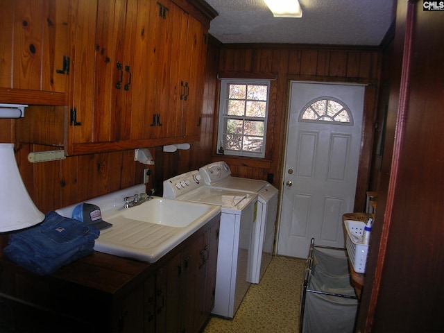 laundry room featuring cabinets, wooden walls, separate washer and dryer, a textured ceiling, and ornamental molding