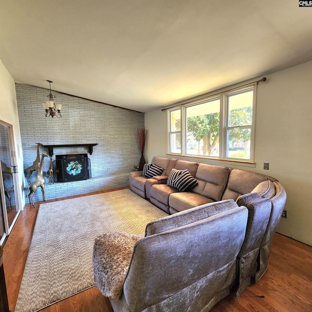 living room with an inviting chandelier, wood-type flooring, vaulted ceiling, and a brick fireplace