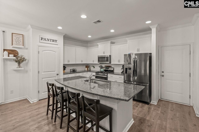 kitchen with a kitchen breakfast bar, dark stone counters, stainless steel appliances, light hardwood / wood-style flooring, and white cabinetry