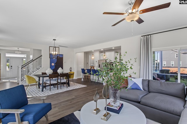 living area with stairs, ceiling fan with notable chandelier, plenty of natural light, and wood finished floors