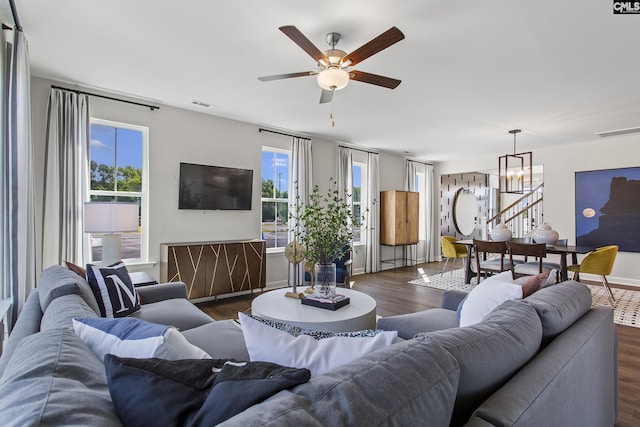 living room with visible vents, stairway, dark wood-type flooring, and ceiling fan with notable chandelier