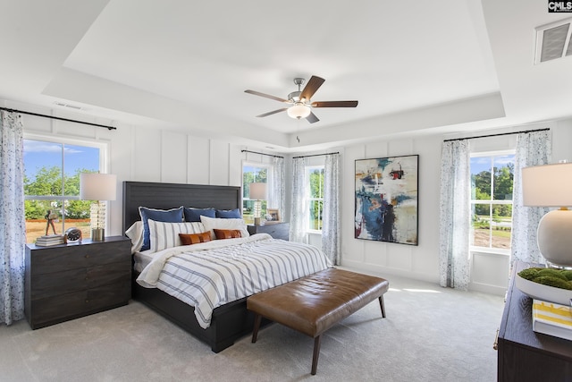 bedroom featuring light carpet, multiple windows, visible vents, and a tray ceiling