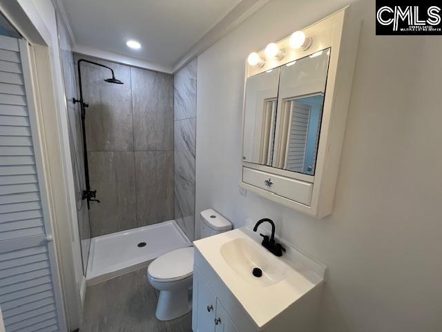 bathroom featuring toilet, a tile shower, and vanity