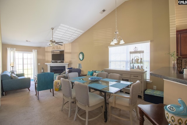 carpeted dining area with ceiling fan with notable chandelier and high vaulted ceiling