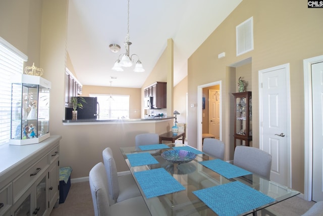 carpeted dining area featuring a notable chandelier and high vaulted ceiling