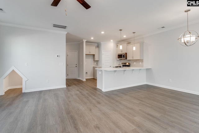 kitchen with white cabinetry, hanging light fixtures, a breakfast bar area, appliances with stainless steel finishes, and light wood-type flooring