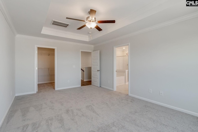 unfurnished bedroom featuring light carpet, a walk in closet, ornamental molding, a tray ceiling, and ceiling fan