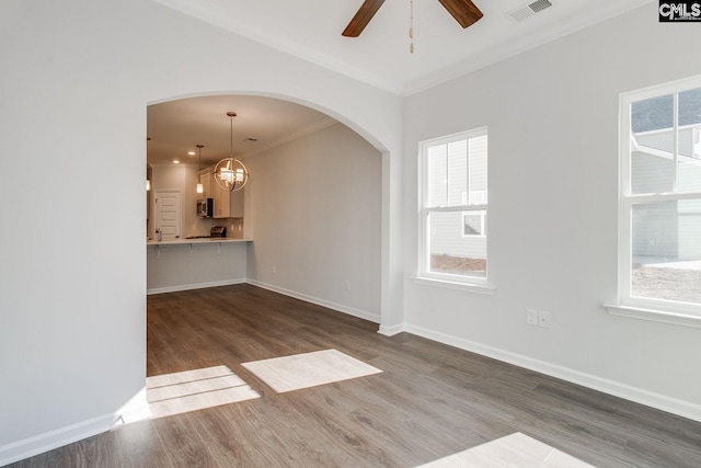 unfurnished living room with a wealth of natural light, dark wood-type flooring, visible vents, and baseboards