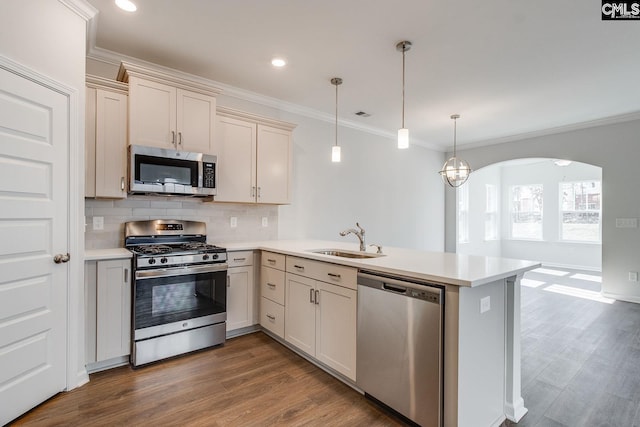 kitchen featuring arched walkways, a peninsula, a sink, light countertops, and appliances with stainless steel finishes