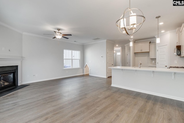 unfurnished living room with ceiling fan with notable chandelier, a glass covered fireplace, crown molding, and wood finished floors