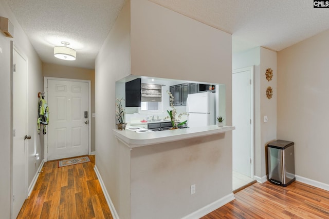 kitchen with kitchen peninsula, white fridge, a textured ceiling, and hardwood / wood-style flooring