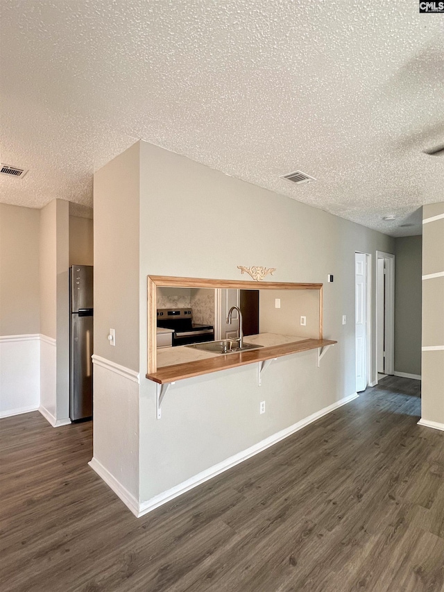 kitchen with a breakfast bar area, dark hardwood / wood-style flooring, range with electric stovetop, and stainless steel fridge