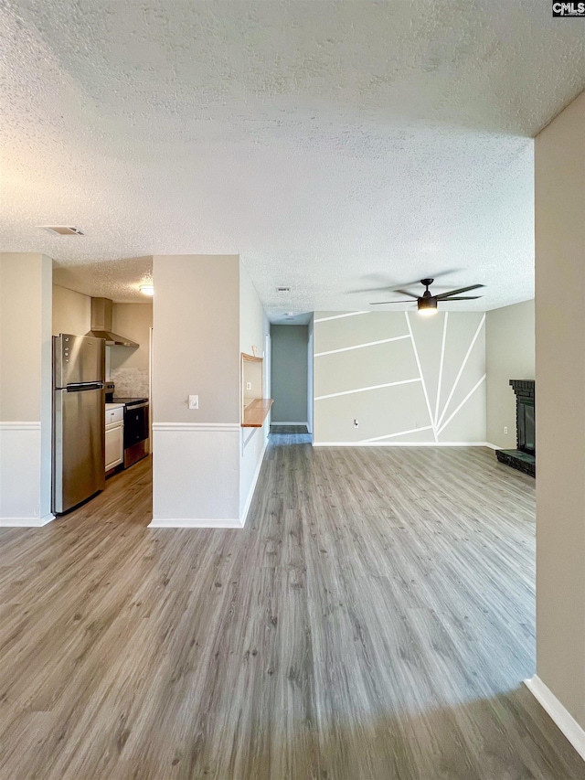 unfurnished living room featuring a textured ceiling, ceiling fan, light hardwood / wood-style floors, and a wood stove