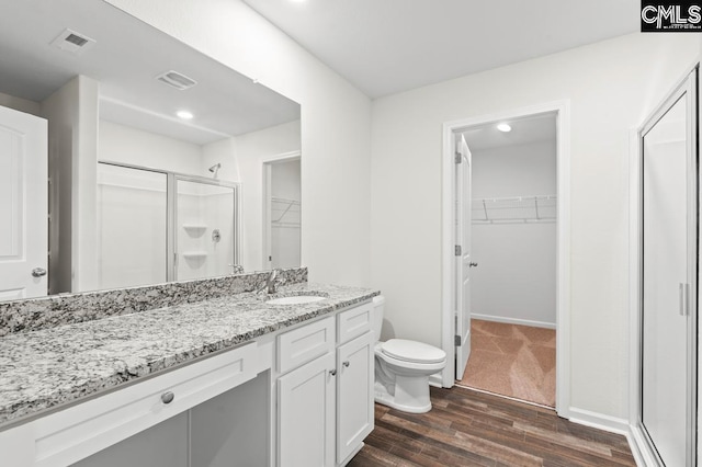 bathroom with wood-type flooring, vanity, toilet, and a shower with door