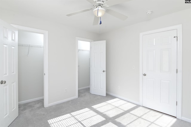 unfurnished bedroom featuring ceiling fan, light colored carpet, and two closets