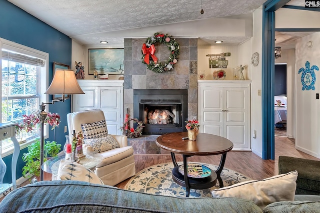 living area featuring a textured ceiling, hardwood / wood-style flooring, vaulted ceiling, and a tiled fireplace