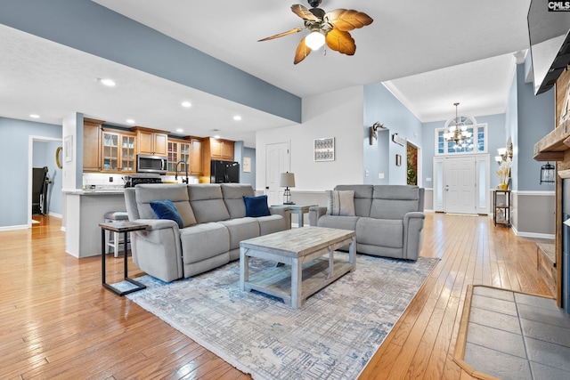 living room featuring ceiling fan with notable chandelier, sink, light wood-type flooring, and ornamental molding