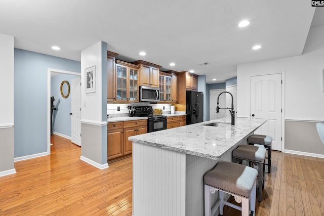 kitchen featuring a kitchen bar, sink, a kitchen island with sink, and black appliances