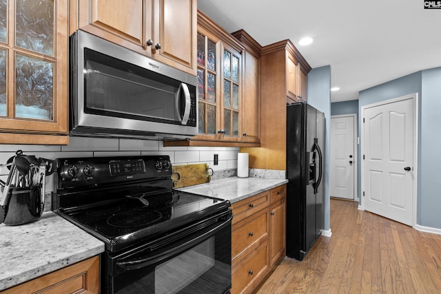 kitchen with decorative backsplash, light stone counters, black appliances, and light hardwood / wood-style floors