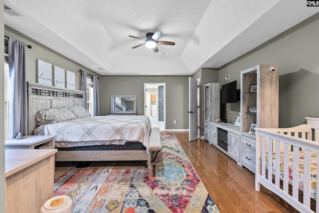 bedroom with hardwood / wood-style floors, a raised ceiling, and ceiling fan