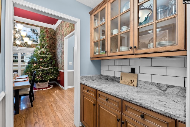 bar with tasteful backsplash, light stone countertops, light hardwood / wood-style floors, and ornamental molding