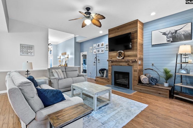 living room with light wood-type flooring, a large fireplace, ceiling fan, and wood walls