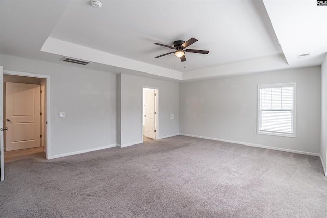 empty room featuring a raised ceiling, ceiling fan, and light carpet