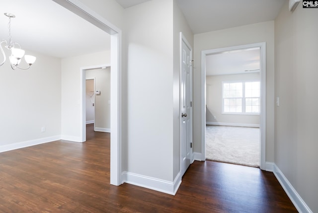 hallway with dark hardwood / wood-style floors and an inviting chandelier