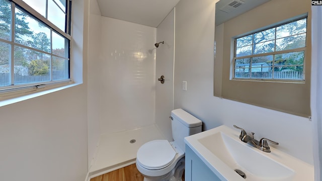 bathroom with hardwood / wood-style floors, vanity, toilet, and tiled shower